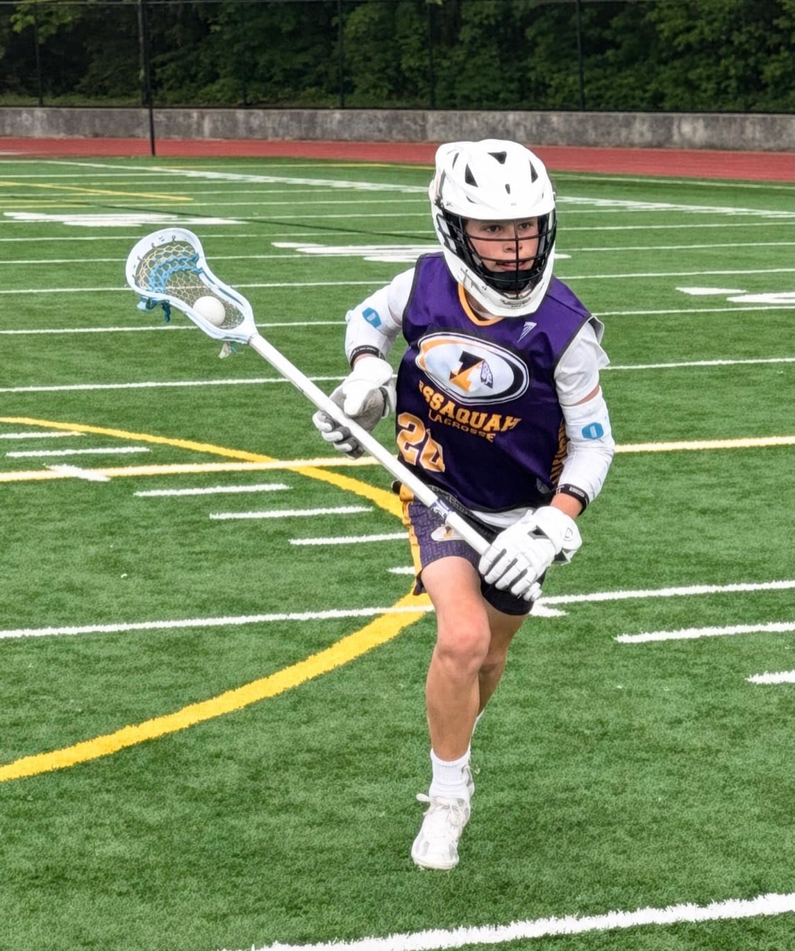 An Issaquah 5/6 player carrying his lacrosse stick on the field.